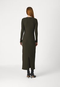 Žebrované, dlouhé rukávy, olivově zelené šaty s rozparkem vzadu. V kombinaci s černými, vysokými botami na podpatku. Jednoduchý, obepnutý design.