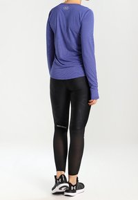 Långärmad lila randig skjorta, svarta åtsittande leggings med texturerade mönster och svarta sportskor. Synlig logotyp på kläderna.