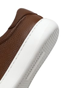Bruin leren sneaker met een gestructureerde bovenkant, witte rubberen zool en stijlvolle lijnen. Witte stiksels aan de zijkant en een gladde neus.