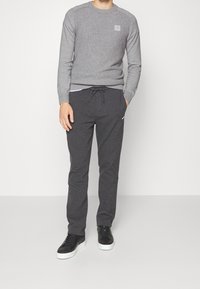 Sweat-shirt gris côtelé à col rond avec patch logo, associé à un pantalon de survêtement gris foncé slim et des baskets basses noires.