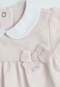 Robe rose clair avec un col Claudine blanc, tissu texturé, un nœud décoratif et de petits détails brillants. Fermeture par pression métallique.
