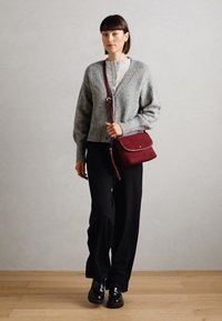 Cardigan gris à côtes avec un col en V, chemise légère à boutons en dessous, pantalon large noir et sac en bandoulière bordeaux. Chaussures en cuir.