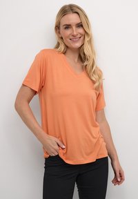 Short-sleeve V-neck t-shirt in a solid orange color, made of soft fabric with a relaxed fit, paired with dark jeans.