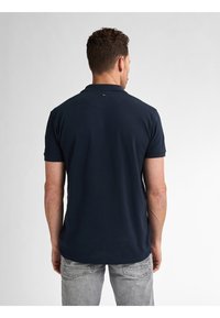 T-paidat navy blue, lyhyet hihat, hillitty kaulus ja pieni logo-etiketti takana, yhdistetty kevyisiin harmaisiin farkkuihin.