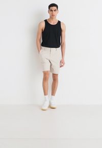 Svart tank topp, beige shorts og hvite sneakers med lyse såler. Enkel design, avslappet passform og nøytral fargepalett.