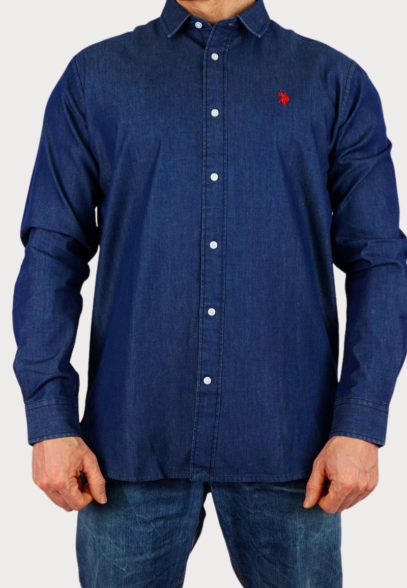 Chemise à manches longues bleu foncé avec des boutons en denim, ornée de boutons blancs et d'un petit logo rouge sur la poitrine.