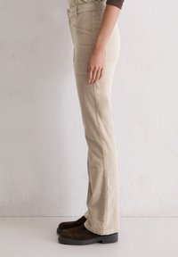 Beige wijde broek met een gestructureerde pasvorm, voorkantzakken en een gladde textuur, gestyled met donkerbruine platform schoenen.