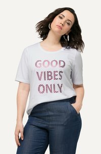 Camiseta blanca de manga corta con "SOLO BUENAS VIBRAS" en letras estriadas rosas. Tela suave, cuello redondo. Combinada con pantalones azul oscuro.