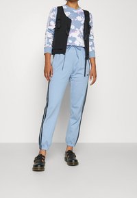Black sleeveless vest, floral pattern sweatshirt in blue and gray, light blue pants with black side stripes, and black leather shoes.
