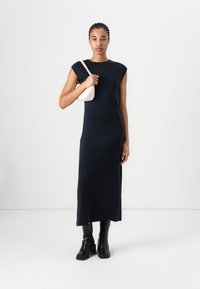 Μάυρη αμάνικη φόρεμα με εφαρμοστή γραμμή, διαγώνιοι ραφές, συνδυασμένο με μικρή ανοιχτό ροζ τσάντα και μαύρες χοντρές μπότες με τακούνι.