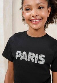 Juoda trumparankovė marška su užrašu "PARIS" didelėmis blizgiomis sidabro spalvos raidėmis. Minkšta medžiaga su nedideliu elastingumu ir apvaliu kaklu.