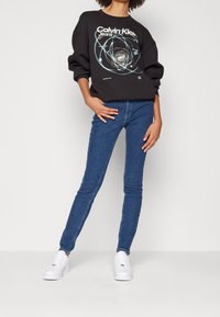 Svart sweatshirt med graphic från Calvin Klein Jeans, kombinerad med blå smala jeans och vita sneakers, med en avslappnad passform och sänkta axlar.