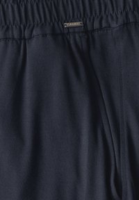 Marineblauwe sweatpants van zacht materiaal, met een elastische tailleband en een klein metalen merklabel. Soepele textuur met minimale stikseldetails.