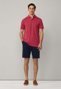 Röd kortärmad polo med krage, kombinerad med mörkblå shorts. Bruna slip-on skor fulländar outfiten.
