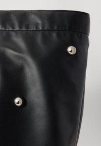 Black leather tote with a textured finish, featuring silver hardware accents and a pleated top edge. Soft appearance with metallic studs.