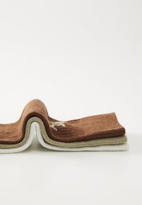 Deux chaussettes en coton pliées, de couleur marron, crème et vert olive. Motif en maille texturée avec un logo blanc sur la chaussette marron.