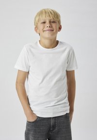 Fehér pamut póló rövid ujjakkal, kerek nyakkivágással és laza szabással, sötét farmernadrággal párosítva. Egyszerű dizájn, nincsenek minták vagy díszítések.