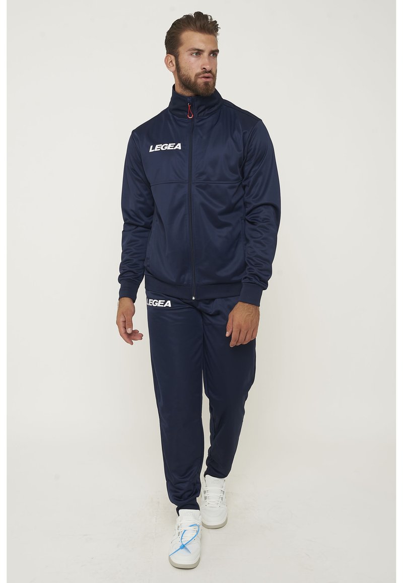Chándal atlético de color navy con chaqueta con cremallera y pantalones a juego. Presenta el logo de LEGEA en blanco, fabricado en un material suave y ligero.