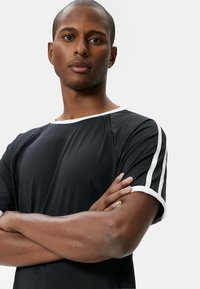 Zwarte t-shirt met korte mouwen met witte afwerking en dubbele witte strepen op de mouwen; zachte textuur en een ontspannen pasvorm.