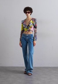 Top curto colorido com decote franzido, estampado em várias cores; combinado com jeans de perna larga azul claro e sandálias pretas.