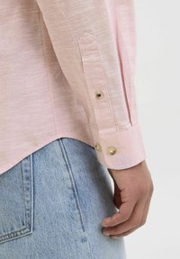 Ljusrosa långärmad skjorta med en texturerad kvalitet och knäppta manschetter. Stylad med ett ljusblått denimplagg, vilket visar en sömlös övergång.