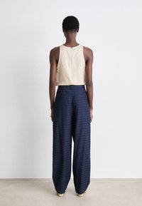 Beige linnen tanktop met ritssluiting aan de achterkant, gecombineerd met donkerblauwe wijde broek met een subtiel gestreept patroon.