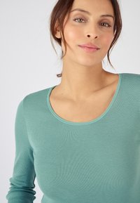 Langdurige, aansluitende top in zacht, geribbeld teal stof met een ronde hals. Bevat subtiele textuur en een gladde afwerking.