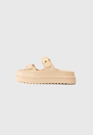 Des sandales à plateforme beige avec deux fermetures à sangles ajustables, une semelle texturée et une finition lisse. Le design présente une pointe arrondie.
