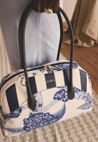 Blå och vit mönstrad handväska i canvas. Har ränder och blommönster, med handtag i svart läder och guldfärgade dragkedjedetaljer.