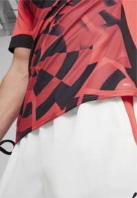 Czerwono-czarny sportowy T-shirt z geometrycznymi wzorami, wyposażony w technologię odprowadzającą wilgoć DRYCELL oraz krótki rękaw.