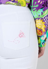 Valkoiset farkut sisältävät takataskun, jossa on vaaleanpunainen brodeerattu mehiläinen ja täplikkään viivan kuvio, mikä korostaa kankaan ainutlaatuisia yksityiskohtia.