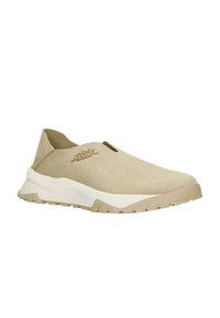 Beige instapper met een zachte suede bovenkant, contrasterende witte tussenzool, gestructureerde gripzool en subtiele merklogo-detail.