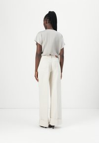 Lichtgrijze top met korte mouwen, gecombineerd met hoogwaist, wijde crème broek met omgeslagen pijpen en achterzakken.