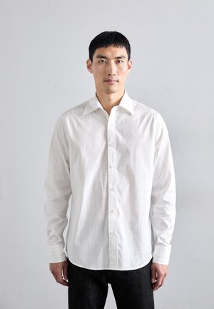 Camisa blanca de vestir con un sutil patrón de cuadrícula, mangas largas y cierre de botones en la parte delantera. La tela parece suave y ligera.