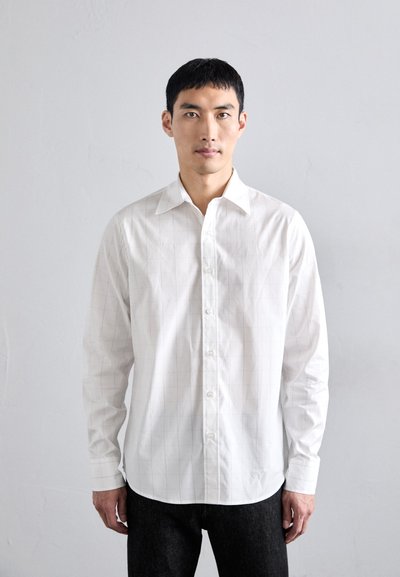 Camisa blanca de vestir con un sutil patrón de cuadrícula, mangas largas y cierre de botones en la parte delantera. La tela parece suave y ligera.