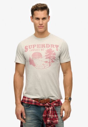 Gray cotton t-shirt featuring a red graphic print of trees and a sun, paired with blue jeans and a red plaid shirt tied around the waist.