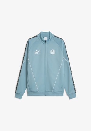 Jasnoniebieska sportowa kurtka rozpinana na zamek z czarnymi i białymi wzorzystymi paskami na rękawach, białym logo Puma i okrągłym emblematem na piersi.
