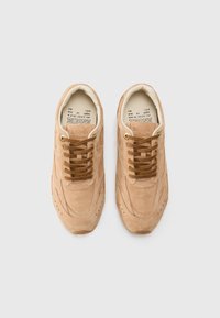 Sneaker beige in suede con punta rotonda, design con lacci e occhielli dorati. Presenta accenti laterali testurizzati e una fodera interna imbottita.