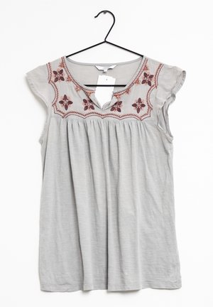 Light gray sleeveless blouse with floral embroidery around round neckline, hanging on black hanger against white background.