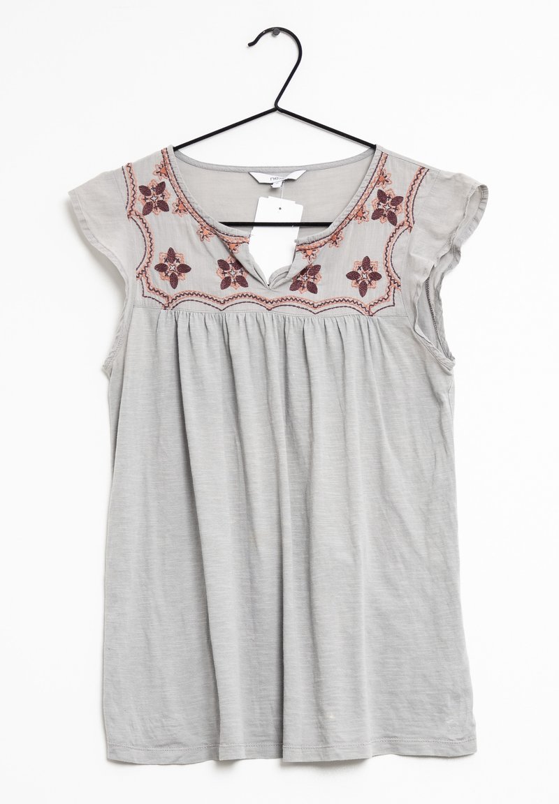 Blouse sans manches gris clair avec broderie florale autour du col rond, suspendue sur un cintre noir sur un fond blanc.