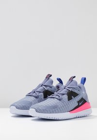 Zapatillas Nike con parte superior de malla en un tono morado claro, acentos en negro, suela rosa y tab de talón azul. Superficie texturizada y cuello acolchado para mayor comodidad.