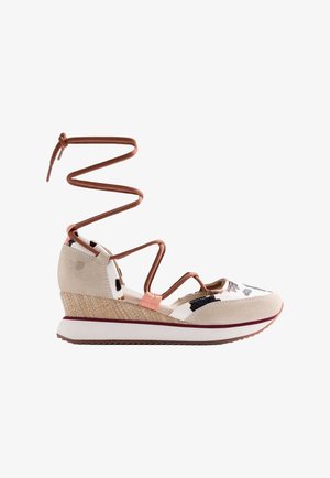 Sandalia cuña beige con tacón de cuña, parte superior estampada, múltiples tiras finas marrones y largos lazos de atar en el tobillo sobre fondo blanco.