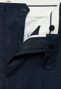 Pantaloni de culoare bleumarin, cu fermoar și închidere cu buton, având un căptușeală interioară de culoare crem și detalii de cusătură contrastante.