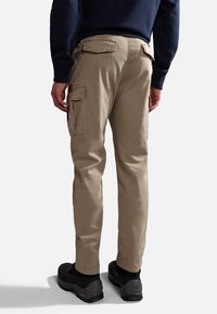 Beżowe spodnie cargo z bocznymi kieszeniami, zapinanymi na guziki kieszeniami z tyłu oraz luźnym krojem. Noszone z czarnymi butami i granatowym swetrem.