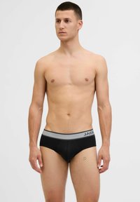 Schwarze Brief-Unterwäsche im Stil mit einem grauen elastischen Bund mit der Aufschrift "JACK". Weiches Material und körpernahe Passform. Glatte Textur, minimale Details.
