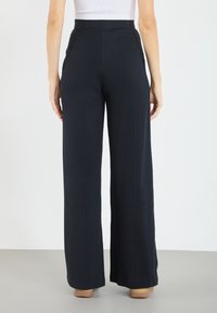 Svarta ribbade vida byxor med hög midja, i en texturerad tyg och en slät finish, visade från baksidan.