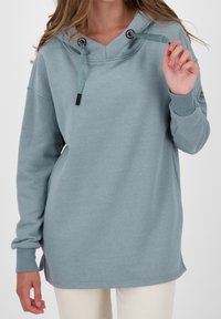 Vaaleansininen huppari, joka on valmistettu puuvillasekoitteesta. Siinä on V-pääntie, säädettävät nyörit, pitkät hihat ja sivuaukollinen muotoilu.