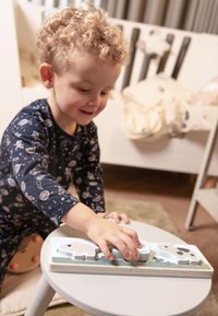 Puzzle en bois avec trois pièces colorées : un cochon rose, une vache noir et blanc, et un mouton blanc, posés sur une table gris clair.