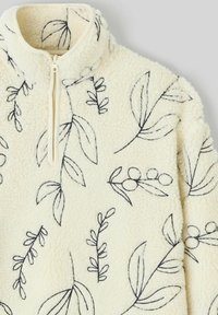 Pull-over en polaire crème avec des motifs de feuilles et de baies brodés en noir, doté d'une courte fermeture éclair à l'avant et d'un col montant.