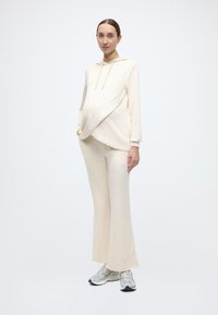 Sweat-shirt à capuche beige avec un design drapé sur un pantalon large assorti, en tissu doux, associé à des baskets grises.